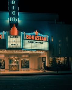 an old movie theater at night with people walking in the street by it and lights on