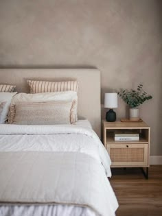 a bed with white sheets and pillows in a bedroom next to a nightstand with a potted plant on it