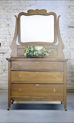 an old dresser with a mirror on top and plants in the bottom drawer, against a white brick wall