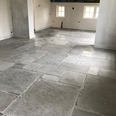 an empty room with stone flooring and two windows on the wall, in front of white walls