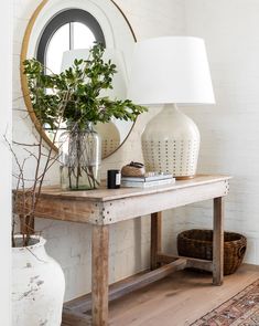 a white table topped with a vase filled with flowers next to a mirror and lamp