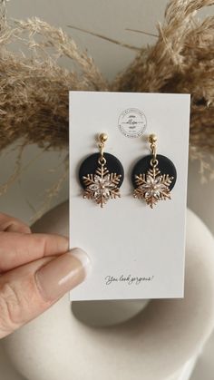 a pair of black and gold snowflake earrings on a card next to some dried grass