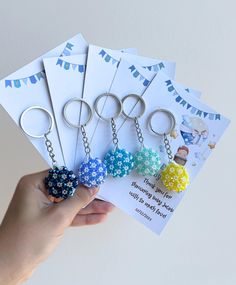 a hand holding five different key chains with flowers on them and a card attached to it