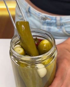 a jar filled with pickles sitting on top of a white table next to a person