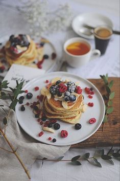 pancakes topped with berries and blueberries on a plate next to a cup of tea