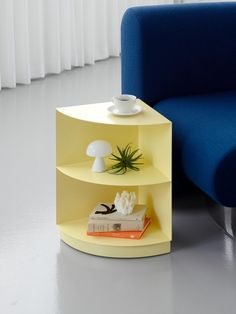 a blue chair next to a yellow shelf with books on it and an air plant