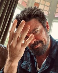 a man holding his hand up to his face while sitting in front of a window