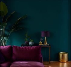 a living room with a purple couch and gold side table in front of a teal green wall