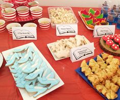 a red table topped with lots of food and desserts covered in frosting on top of plates