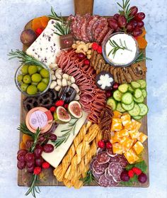 a wooden platter filled with different types of cheeses, meats and fruit