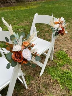 two white chairs sitting on top of a grass covered field next to eachother