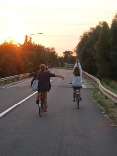 two people riding bikes on a road with the sun setting in the distance behind them