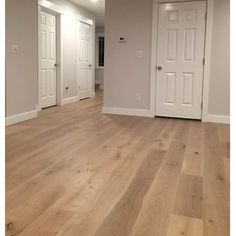 an empty room with white doors and hard wood flooring in the foreground is a hallway leading to another room