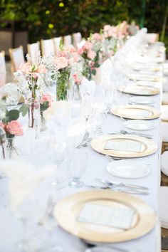 the table is set with white plates and pink flowers in vases on each side