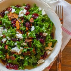 a white bowl filled with salad on top of a table next to a fork and knife