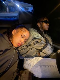 two women sitting in the back seat of a car at night with their eyes closed