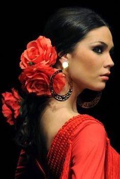 a woman with flowers in her hair wearing earrings and a red dress is looking off into the distance