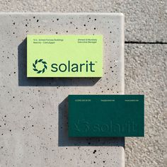 two green business cards sitting on top of a cement wall next to a concrete slab