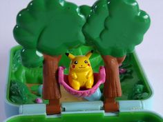 a plastic toy with a yellow pikachu sitting in a hammock between two trees