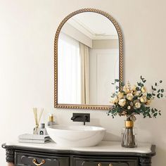 a bathroom with a sink, mirror and flowers on the counter top in front of it