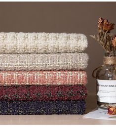 a stack of blankets sitting on top of a table next to a vase with flowers