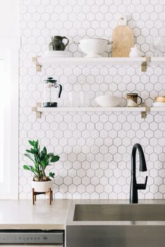 a kitchen with white hexagonal tiles on the wall and shelving above the sink