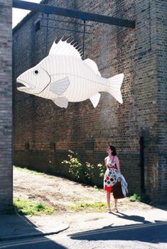 a woman is standing under a paper cut out of a fish on the side of a building