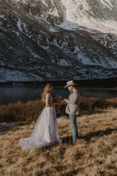 a bride and groom standing in front of a mountain with snow on the mountains behind them