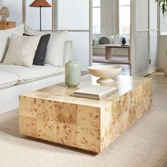 a living room with white couches and wooden table in the foreground is a large window