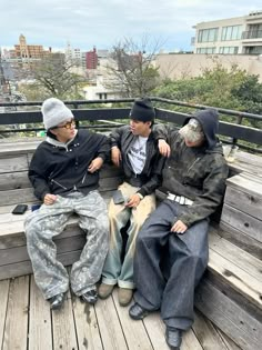 three men sitting on a wooden bench next to each other and one man wearing a beanie