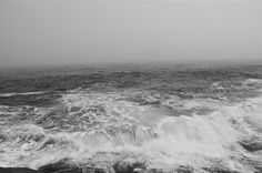 black and white photograph of waves in the ocean on a foggy, overcast day