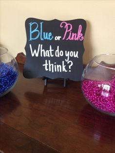 two bowls filled with blue and pink beads on top of a wooden table next to a sign