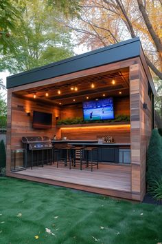 a backyard bar with an outdoor grill and television on the wall, surrounded by lush green grass