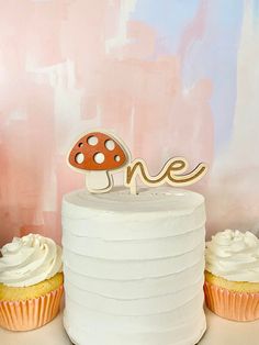 two cupcakes sitting on top of a white cake next to a mushroom shaped one