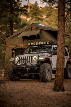 a jeep parked in the woods with a tent attached to it's back end