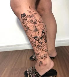 a woman's leg with flowers and butterflies on it, while she is wearing leopard shoes