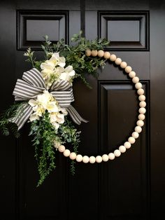 a wreath with white flowers and greenery hanging on a black front door decorated with pearls