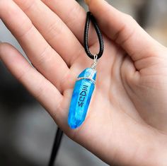 a hand holding a small blue pendant with the word nil on it's side