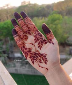 a woman's hand with henna tattoos on it and trees in the background