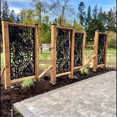 three wooden gates with decorative designs on them in a garden area next to a brick walkway