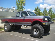 a red and black truck parked in a parking lot next to a house on a sunny day