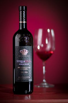 a bottle of red wine next to a glass on a table with a pink background