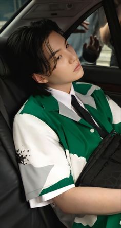 a person sitting in a car wearing a green and white shirt, black tie and holding a laptop