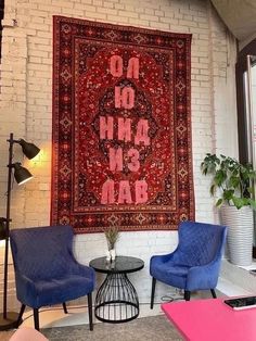 two blue chairs are in front of a red rug on the wall and a black table