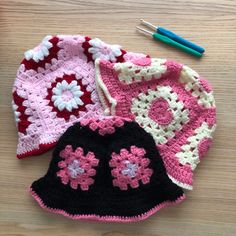 three crocheted hats sitting on top of a wooden table next to knitting needles