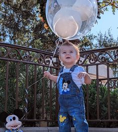 a little boy standing in front of a mickey mouse balloon