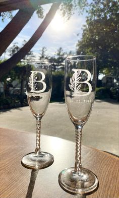 two wine glasses with the letter b on them sitting on a table in front of a tree