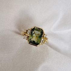 a ring with a green and white stone surrounded by three diamonds on a white cloth