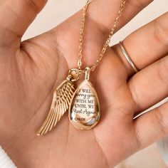 a person holding a gold necklace with an angel wing on it