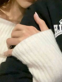 a woman wearing a black shirt and white sweater holding onto her arm with one hand